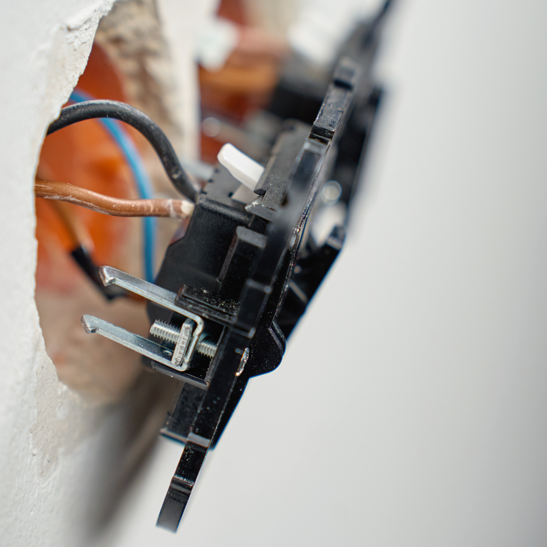 Nærbillede af stikkontakt under installation med synlige ledninger i væggen.